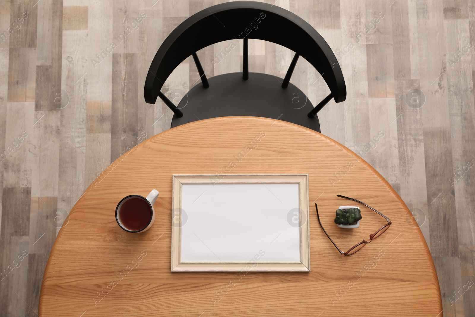 Photo of Round wooden table with cup of tea, photo frame, houseplant and eyeglasses near black chair indoors, top view