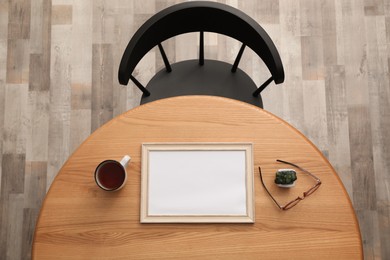 Photo of Round wooden table with cup of tea, photo frame, houseplant and eyeglasses near black chair indoors, top view