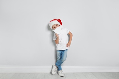 Cute little boy with Santa hat and white beard prop near white wall. Christmas celebration