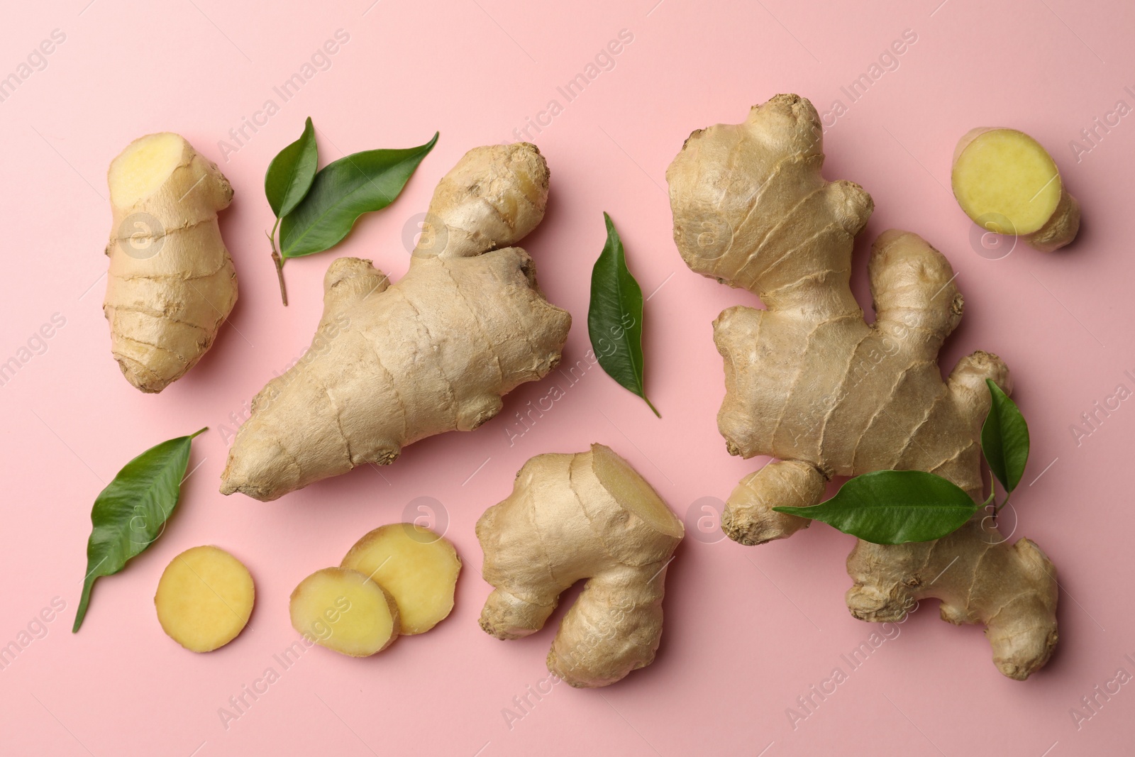 Photo of Fresh ginger with green leaves on pale pink background, flat lay