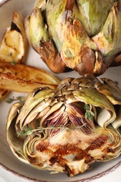 Bowl with tasty grilled artichokes on table, closeup