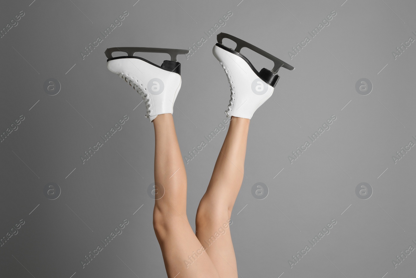 Photo of Woman in elegant white ice skates on grey background, closeup of legs