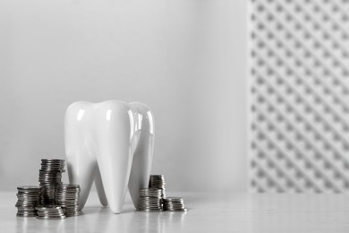 Photo of Ceramic model of tooth and coins on white table, space for text. Expensive treatment