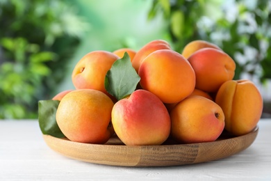 Many fresh ripe apricots on white table against blurred background