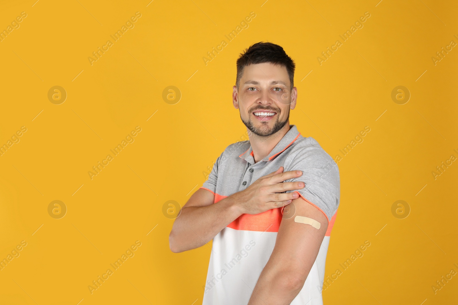 Photo of Vaccinated man showing medical plaster on his arm against yellow background. Space for text