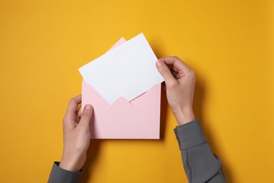 Photo of Woman taking card out of letter envelope at orange table, top view. Space for text