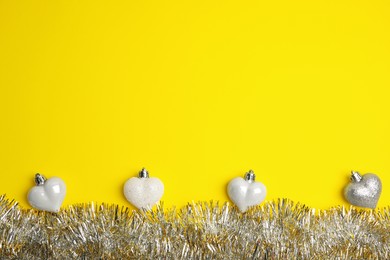 Shiny tinsel and Christmas baubles on yellow background, flat lay. Space for text