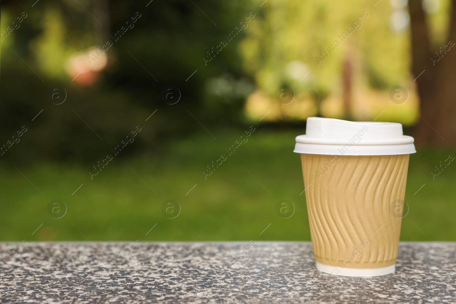 Photo of Paper cup on parapet in park, space for text. Coffee to go