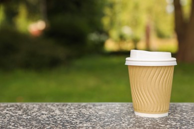 Photo of Paper cup on parapet in park, space for text. Coffee to go