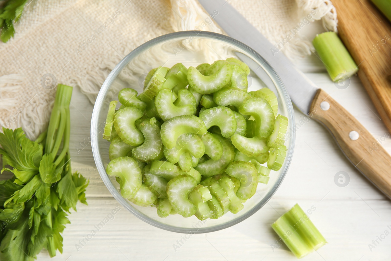 Photo of Cut fresh green celery in bowl on white wooden table, flat lay