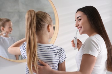 Photo of Mother and her daughter brushing teeth together near mirror in bathroom