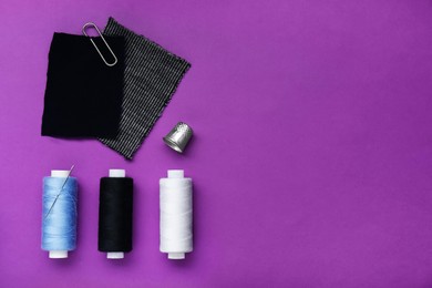 Flat lay composition with thimble and different sewing tools on purple background, space for text