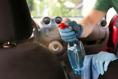 Photo of Man cleaning car salon with disinfectant spray and cloth, closeup