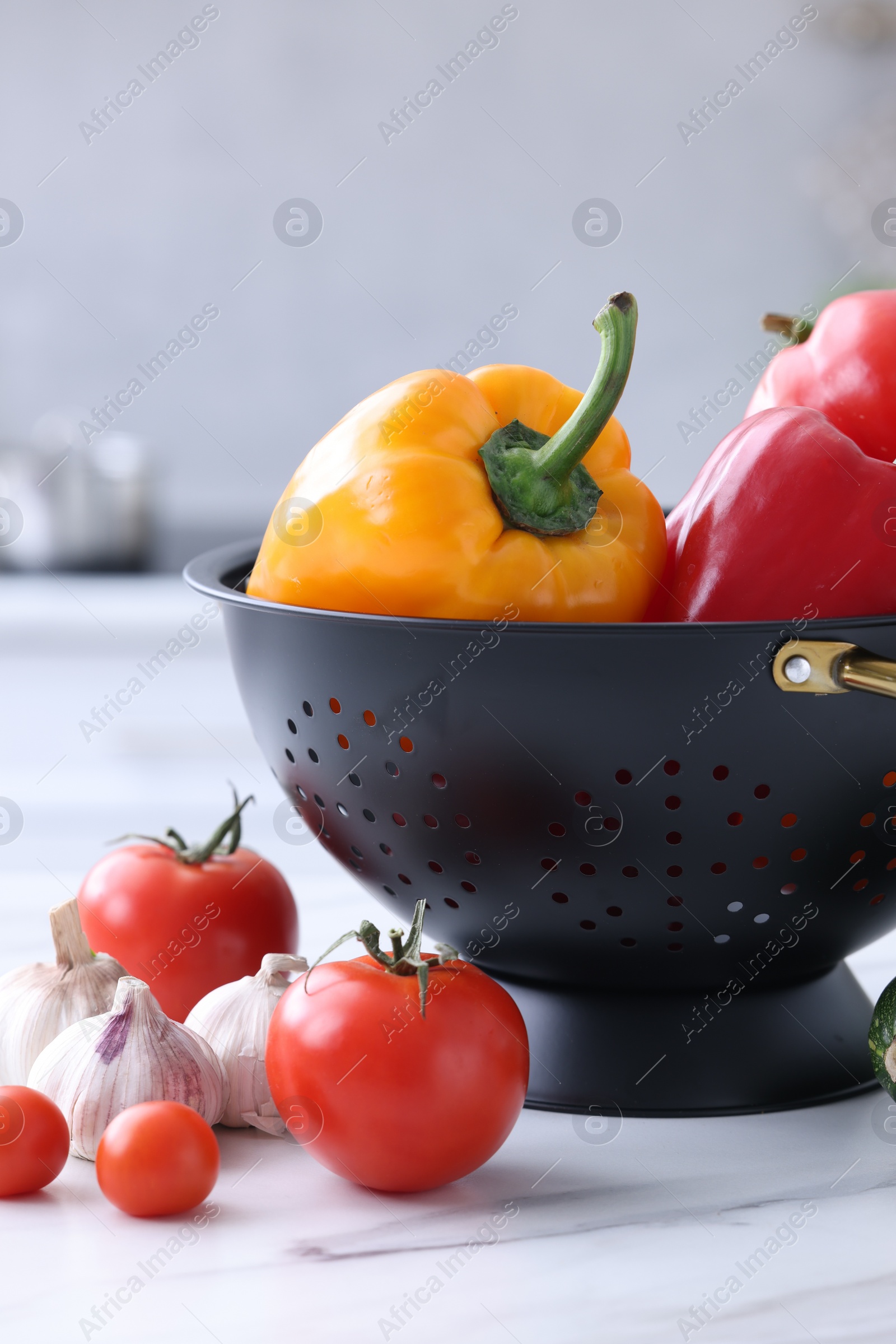 Photo of Black colander and different vegetables on white marble table indoors, closeup