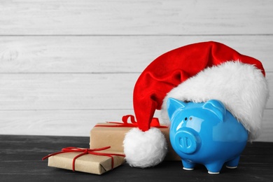 Piggy bank with Santa hat and gift boxes on black wooden table. Space for text