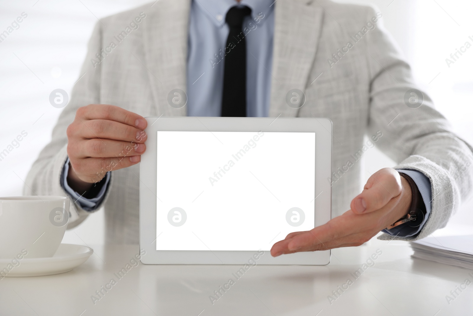 Photo of Businessman holding modern tablet with blank screen at white table in office, closeup