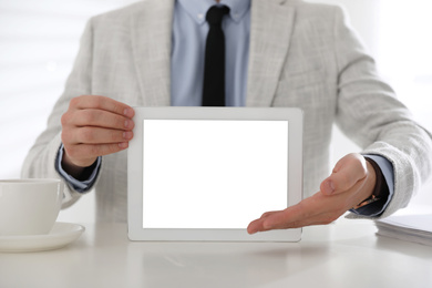 Photo of Businessman holding modern tablet with blank screen at white table in office, closeup