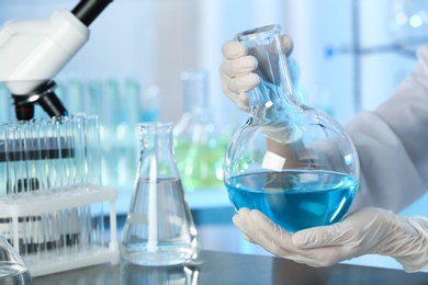Doctor holding Florence flask with blue liquid at table, closeup. Laboratory analysis