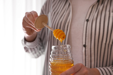 Photo of Woman with honey and dipper indoors, closeup
