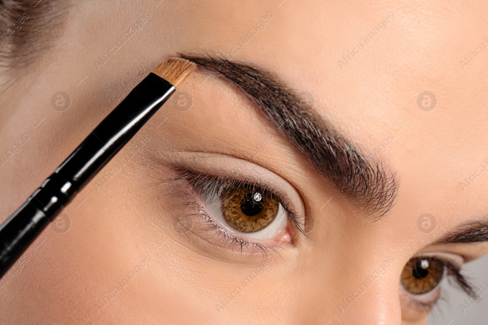 Photo of Young woman correcting eyebrow shape with brush, closeup