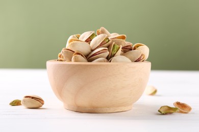 Tasty pistachios in bowl on white wooden table against olive background, closeup