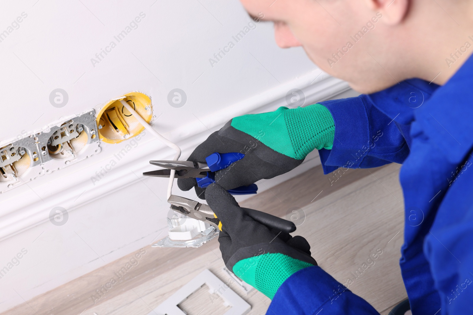 Photo of Professional repairman fixing power sockets with pliers indoors, closeup