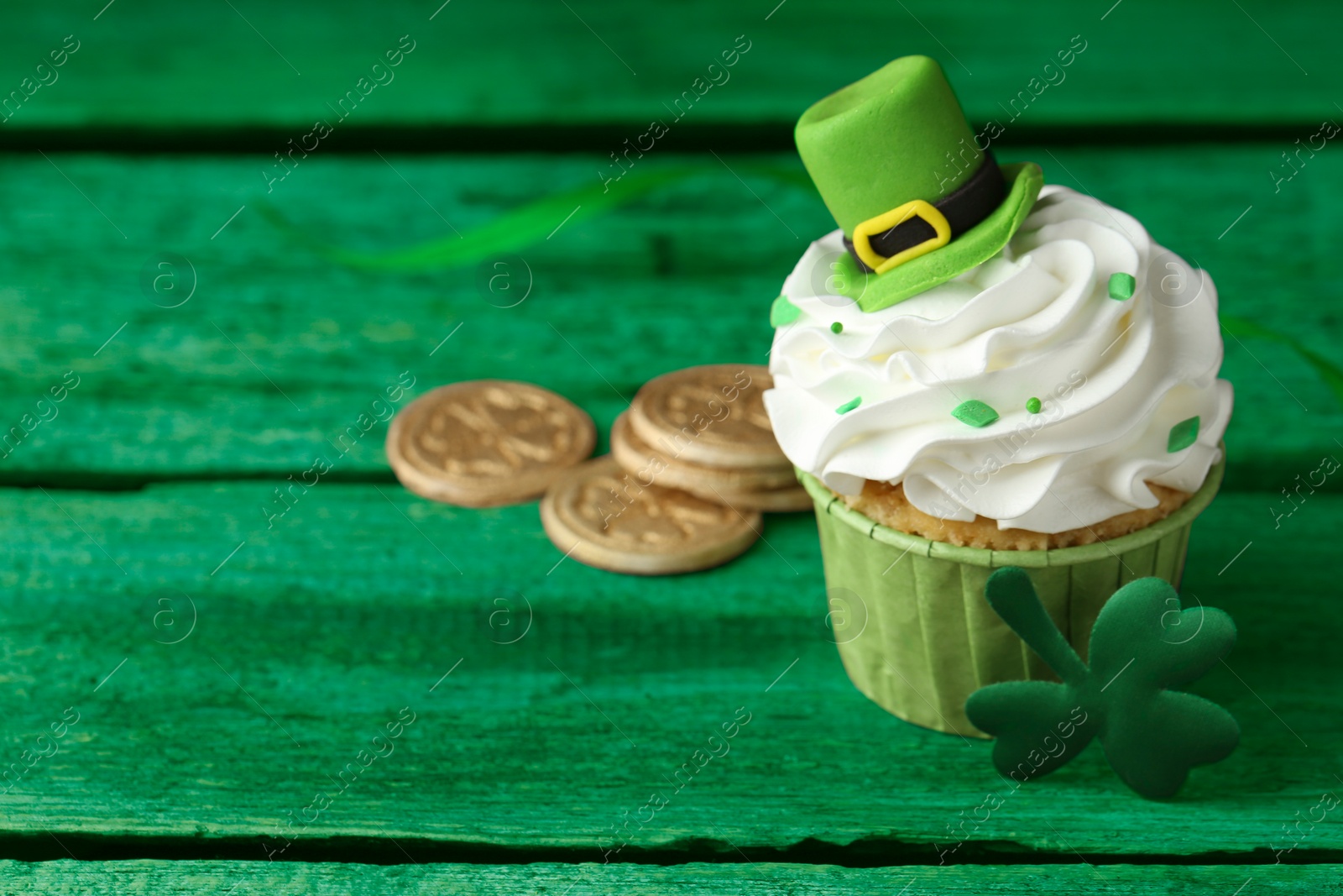 Image of St. Patrick's day. Tasty cupcake with leprechaun hat topper on green wooden table, closeup. Space for text