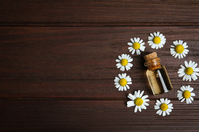 Bottle of essential oil and chamomiles on wooden table, flat lay. Space for text