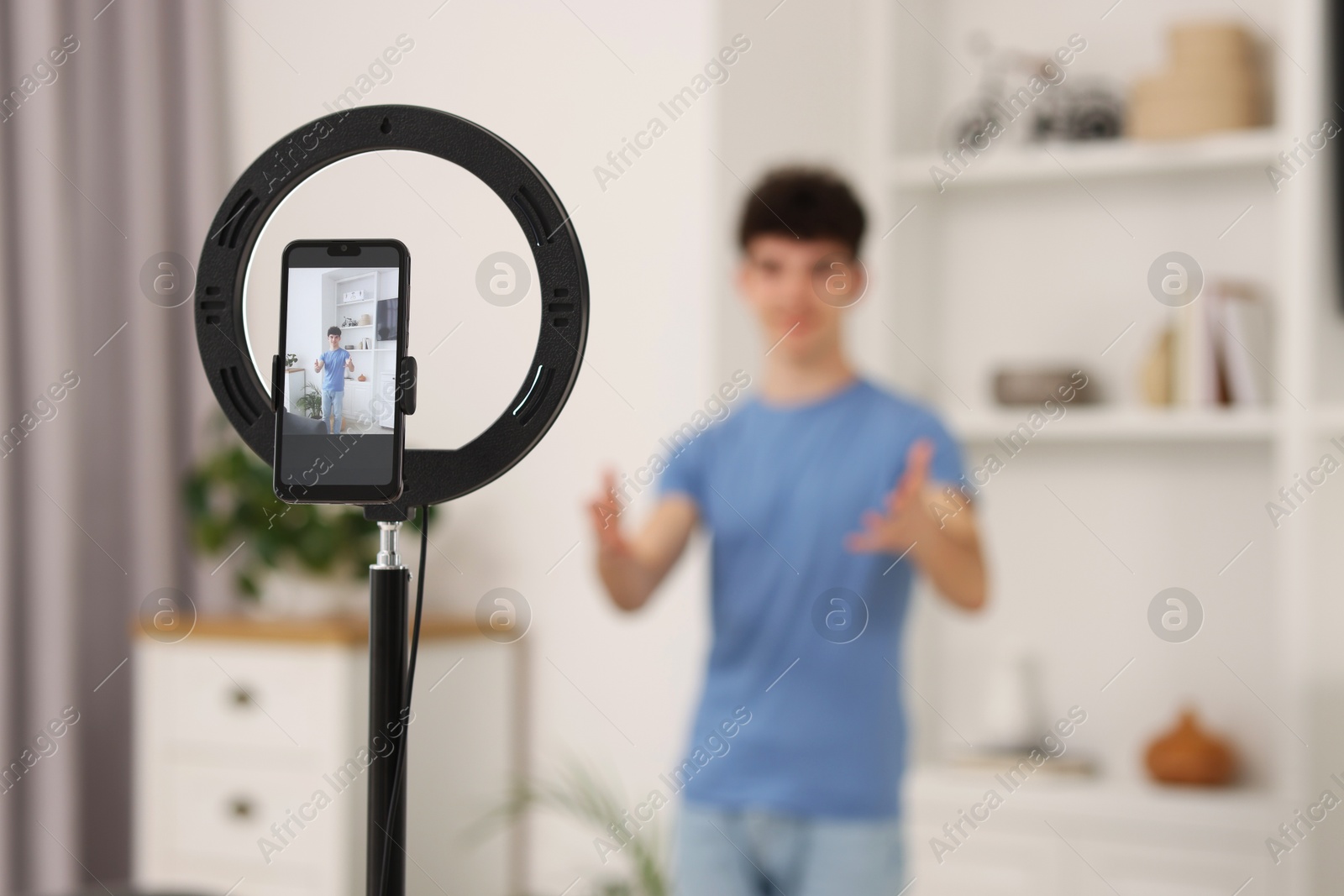 Photo of Teenage blogger explaining something while streaming at home, focus on smartphone