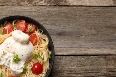 Photo of Delicious spaghetti with burrata cheese and tomatoes on wooden table, top view. Space for text