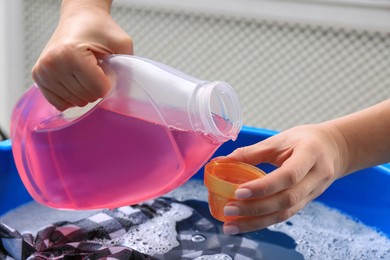 Photo of Woman pouring detergent into cap over basin with clothing, closeup. Hand washing laundry