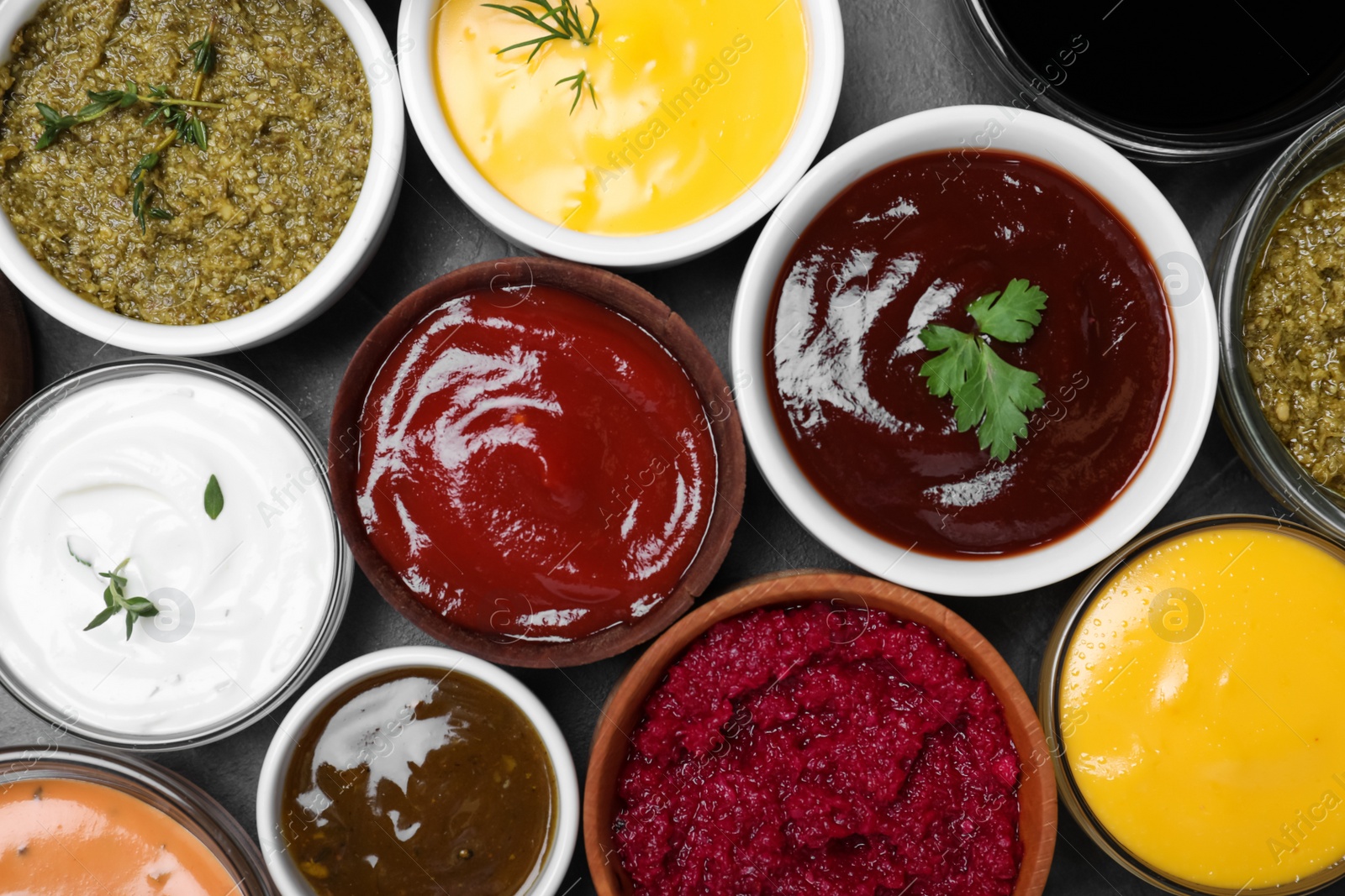 Photo of Many different sauces and herbs on black table, flat lay