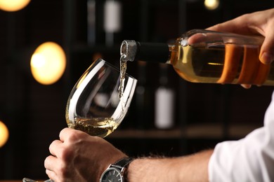 Man pouring white wine into glass indoors, closeup