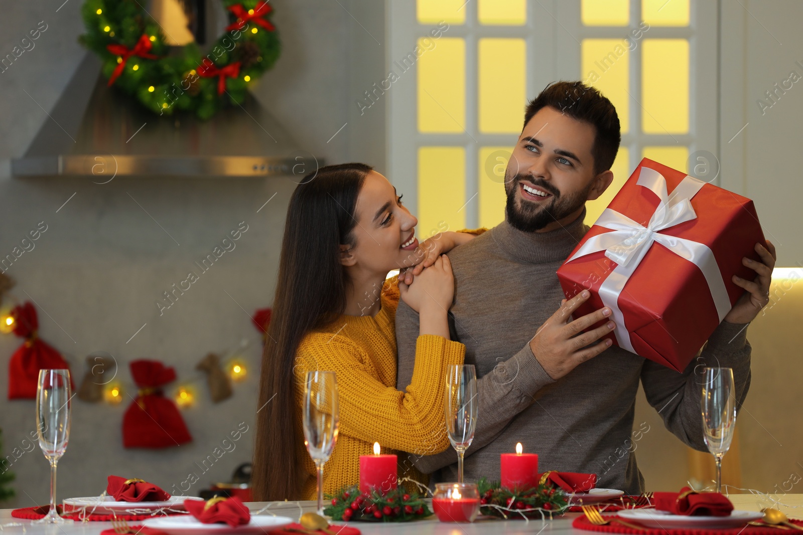 Photo of Happy young man with Christmas gift from his girlfriend at table in kitchen