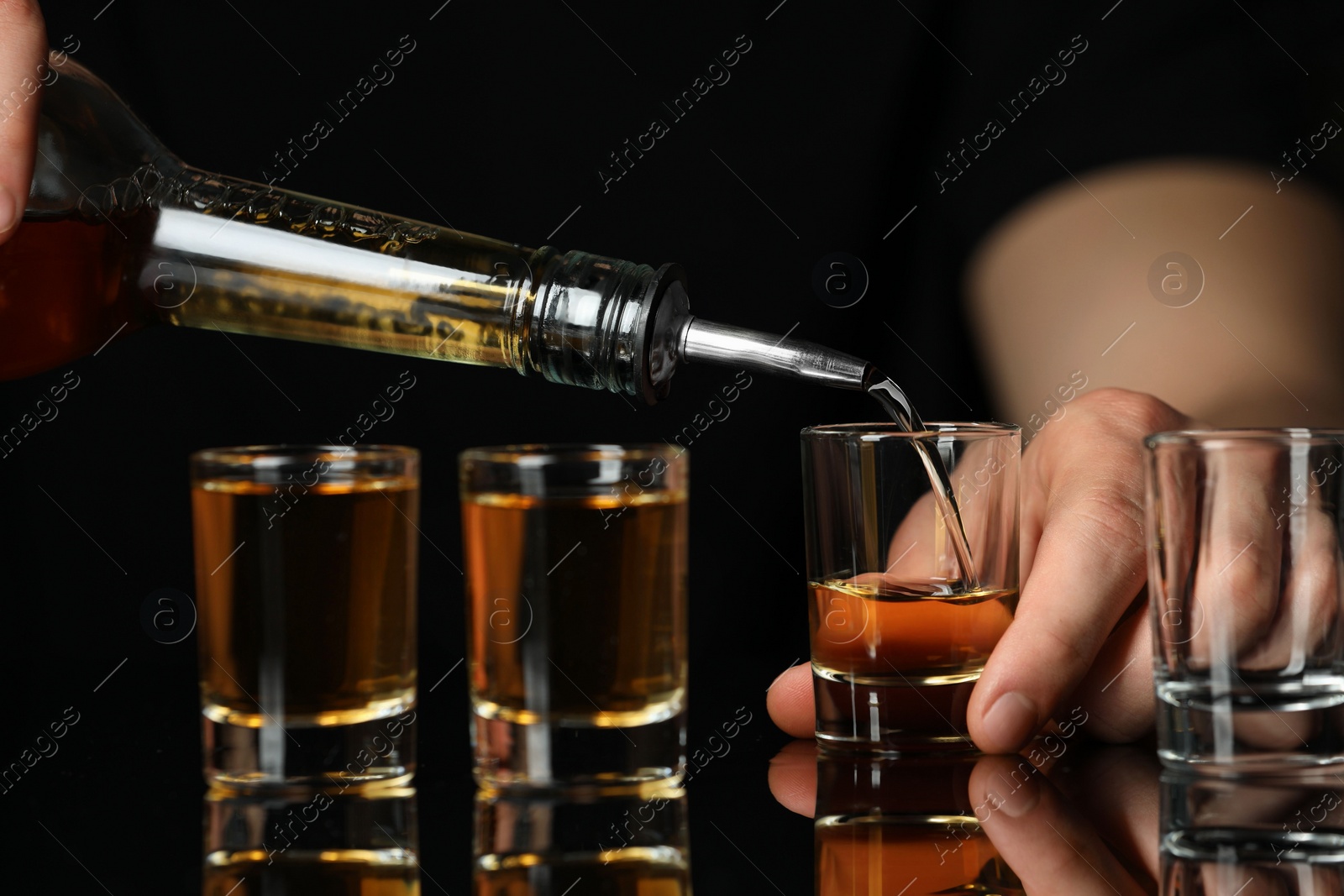 Photo of Bartender pouring alcohol drink into shot glass at mirror bar counter, closeup