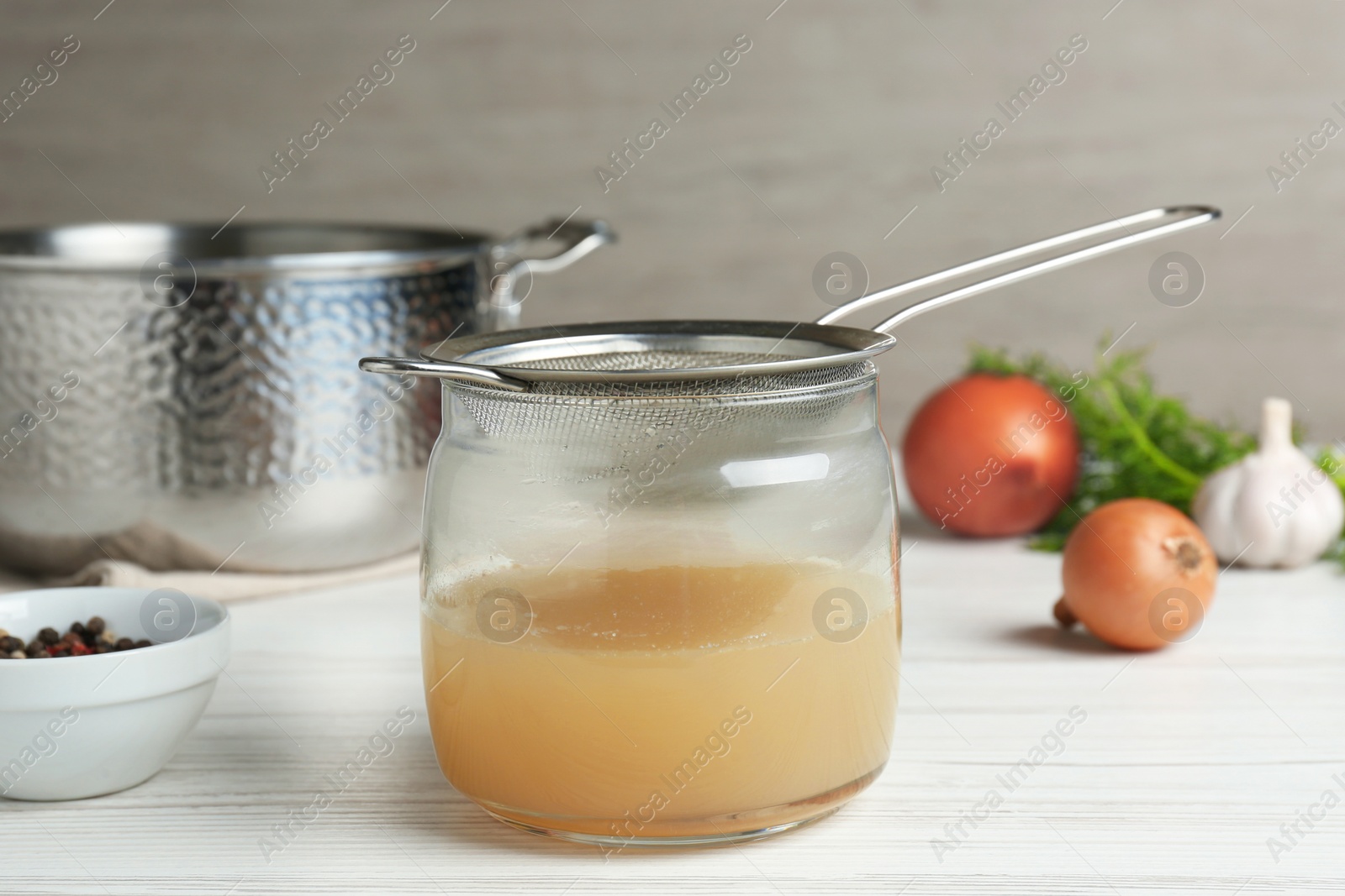 Photo of Straining delicious broth through sieve on white wooden table