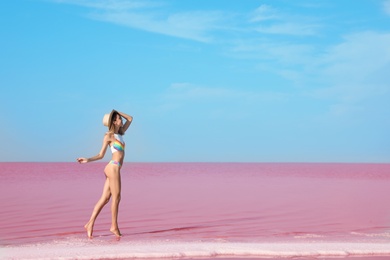 Photo of Beautiful woman in swimsuit standing near pink lake on sunny day