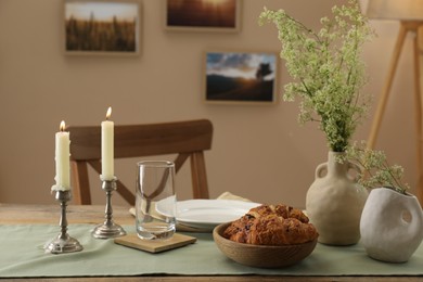 Photo of Clean tableware, candlesticks, flowers and fresh pastries on table in stylish dining room