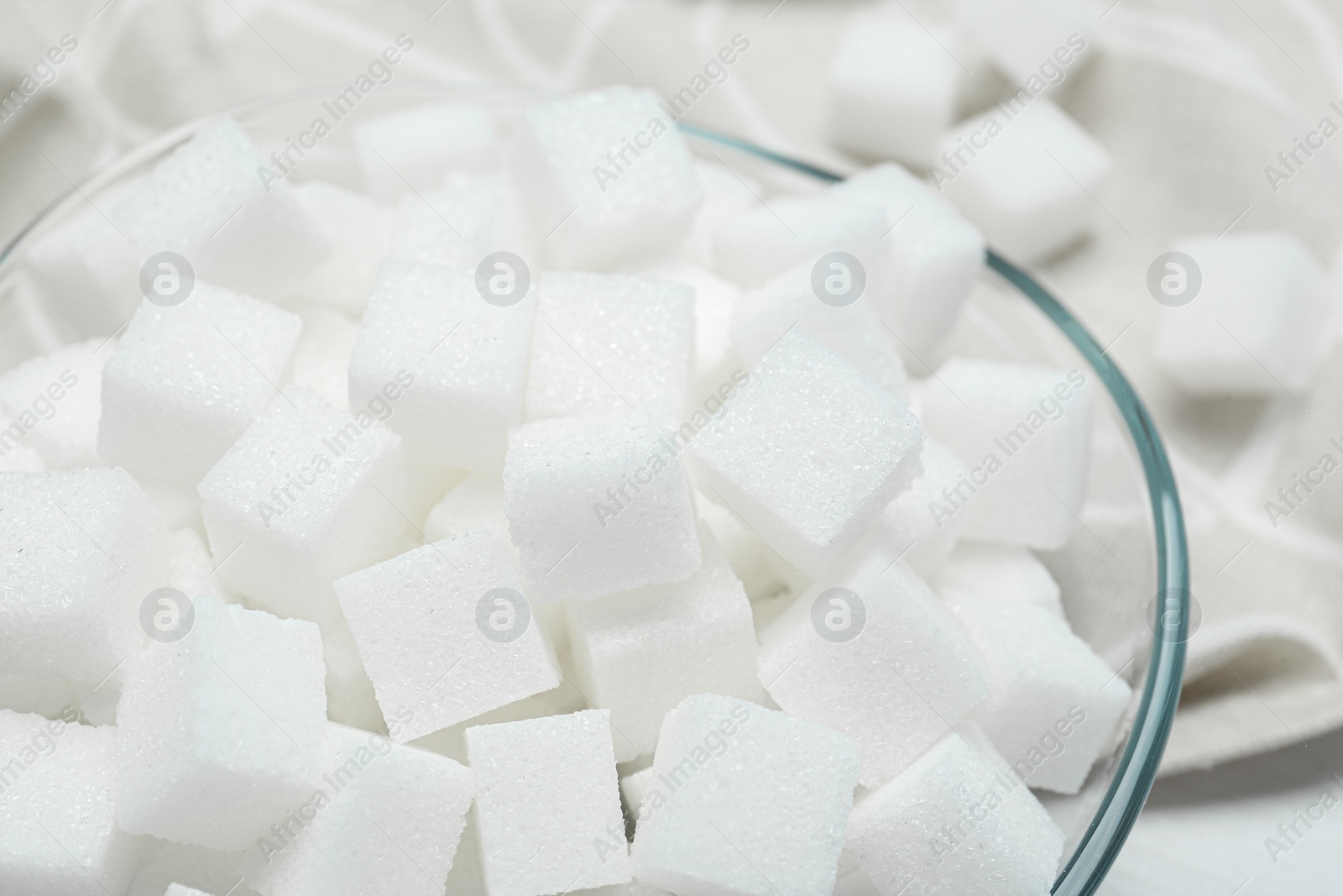 Photo of Many sugar cubes in glass bowl on white wooden table, closeup