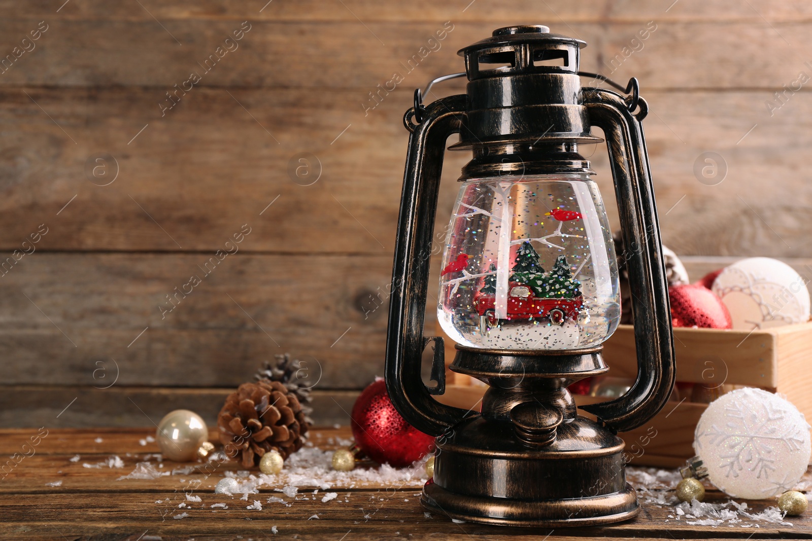 Photo of Beautiful Christmas snow globe in vintage lantern and festive decor on wooden table. Space for text