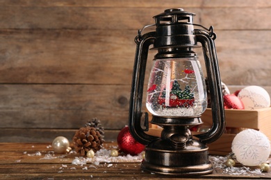 Photo of Beautiful Christmas snow globe in vintage lantern and festive decor on wooden table. Space for text