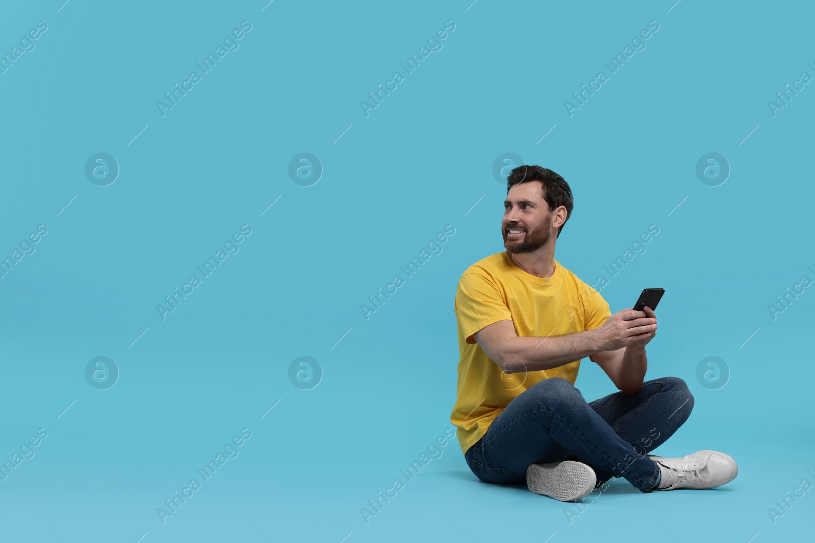 Photo of Smiling man with smartphone on light blue background. Space for text