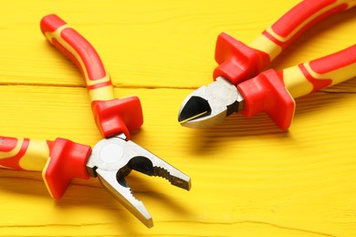 Pliers on yellow wooden table, closeup view