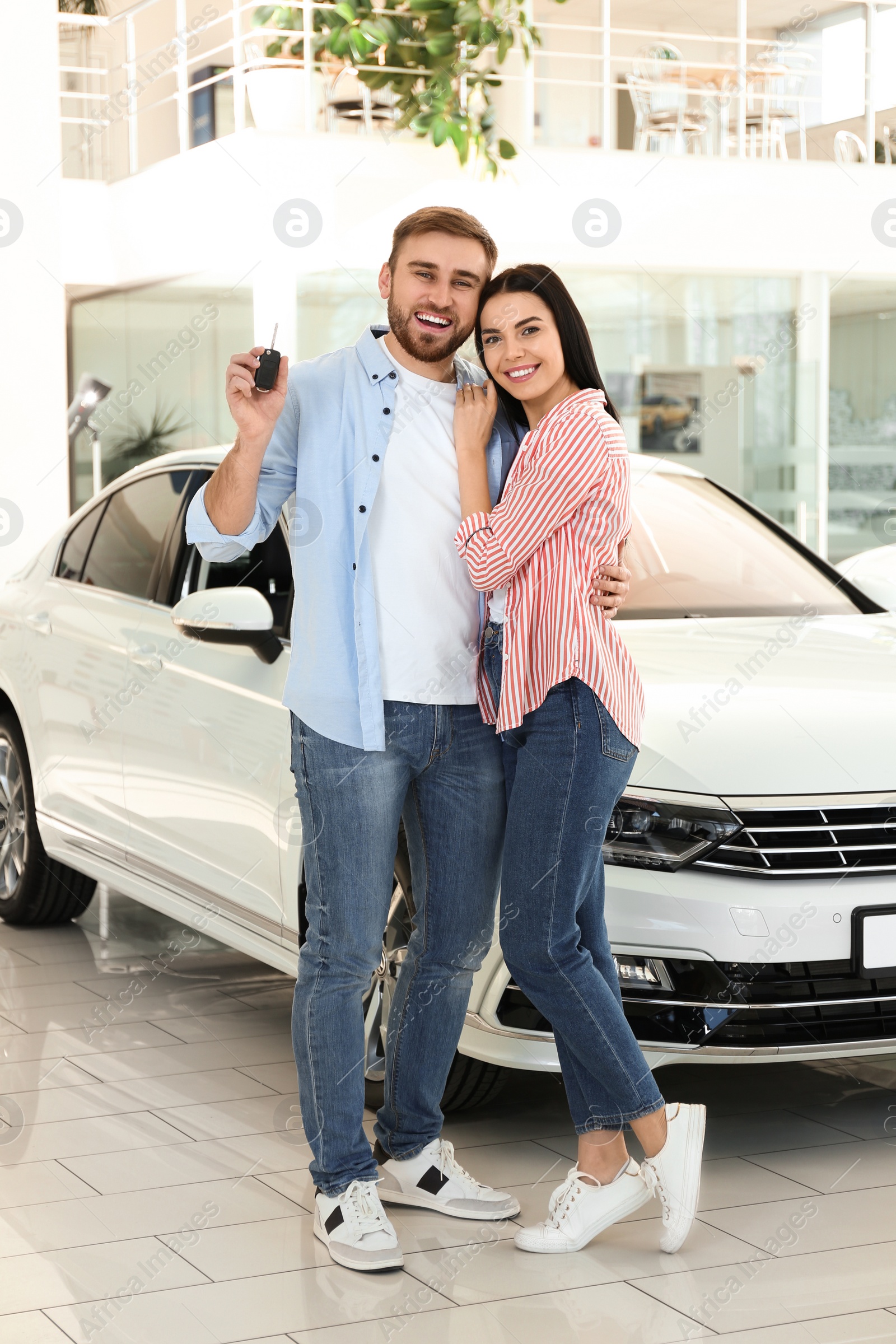 Photo of Happy couple with car key in modern auto dealership