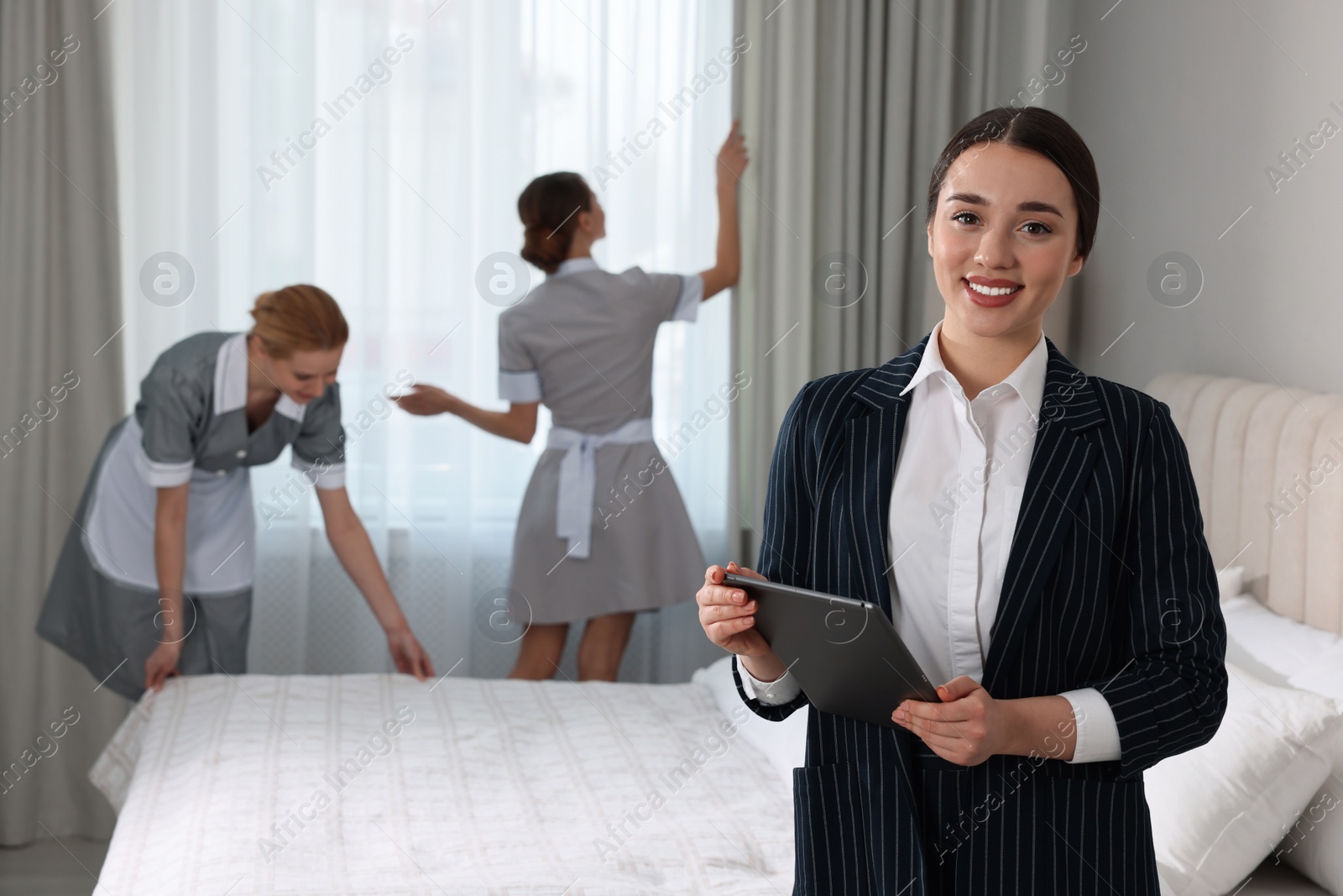 Photo of Housekeeping manager with tablet checking maid's work in hotel bedroom