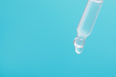 Photo of Dripping serum from pipette on light blue background, closeup. Space for text