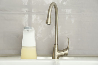 Photo of Modern automatic soap dispenser near sink indoors