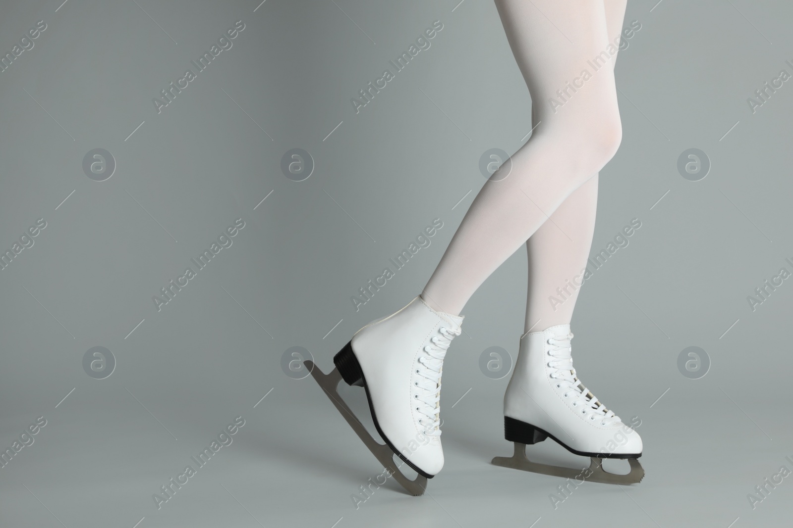 Photo of Woman in elegant white ice skates on grey background, closeup of legs. Space for text