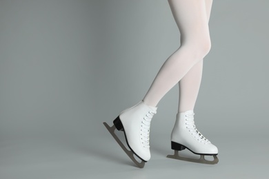 Photo of Woman in elegant white ice skates on grey background, closeup of legs. Space for text