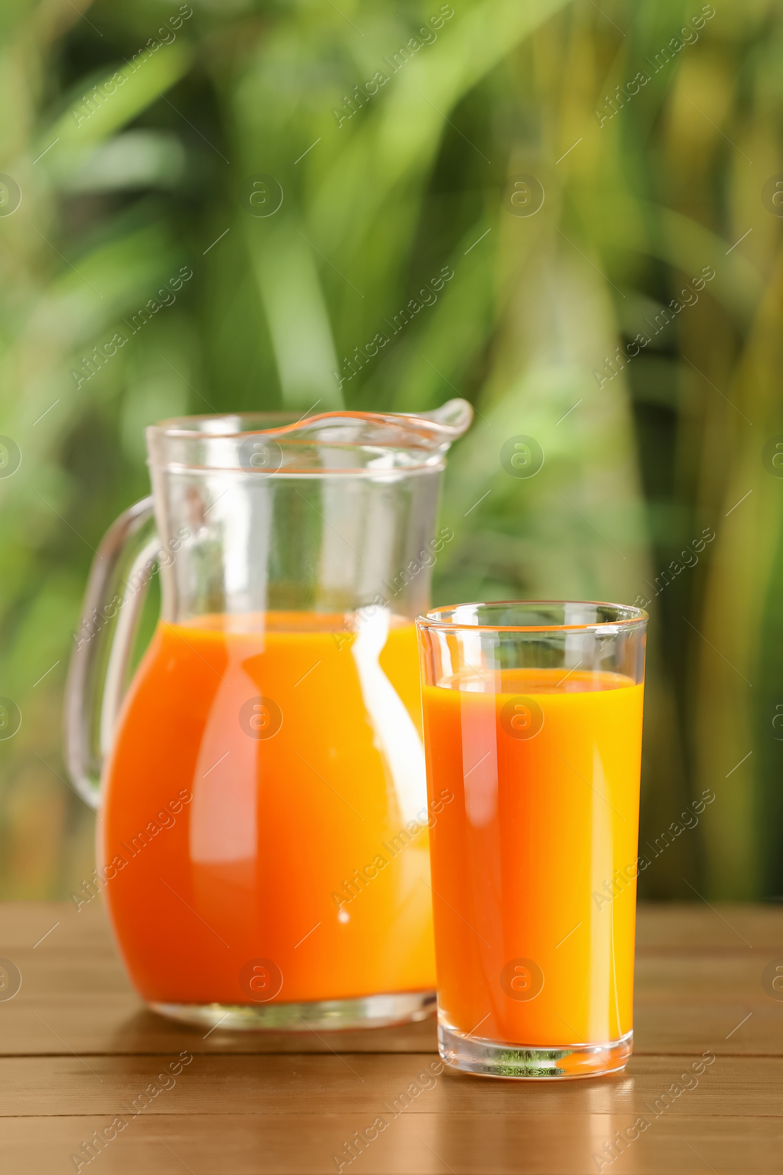 Photo of Tasty refreshing carrot juice on wooden table outdoors